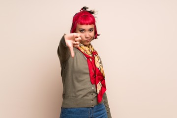 Young woman with pink hair over yellow wall showing thumb down with negative expression