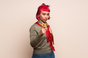 Young woman with pink hair over yellow wall frustrated and pointing to the front