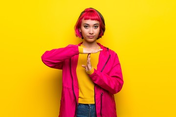 Young woman with pink hair over yellow wall making time out gesture