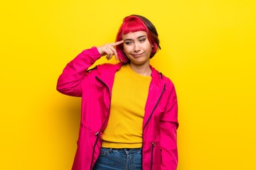 Young woman with pink hair over yellow wall making the gesture of madness putting finger on the head