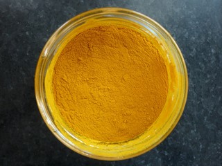 Close up top view of turmeric (curcuma) yellow powder in a glass jar isolated on black granite marble