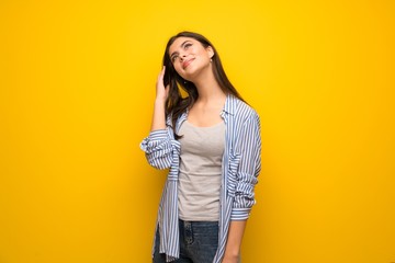 Teenager girl over yellow wall thinking an idea while scratching head