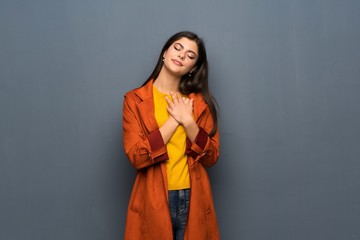 Teenager girl with coat over grey wall having a pain in the heart