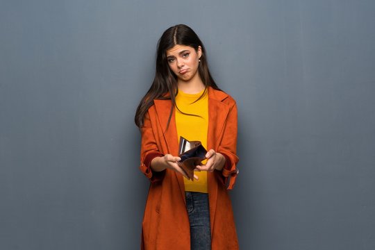 Teenager girl with coat over grey wall holding a wallet