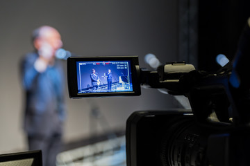Video shooting of the event. Camcorder with LCD display. 2 men on stage in front of microphones on...