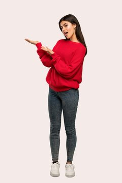 A full-length shot of a Teenager girl with red sweater extending hands to the side for inviting to come over isolated background