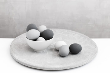Gray eggs lie in a white bowl on a gray background. Gradient color from white to black. Minimal easter concept.