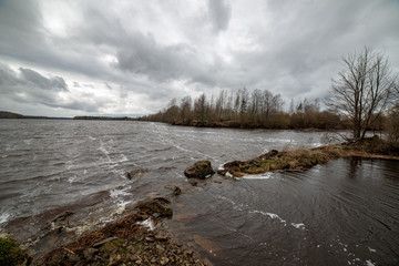 riverside landscape in latvia with dark water and dirty shore line