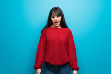 Woman with red sweater over blue wall with surprise facial expression