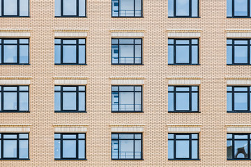 A part of a yellow brick wall with a group of blue windows with reflections. Horizontal texture of...