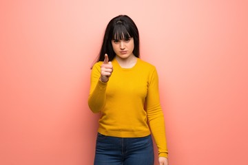 Woman with yellow sweater over pink wall frustrated and pointing to the front