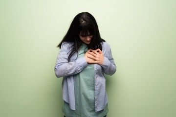 Young woman over green wall having a pain in the heart