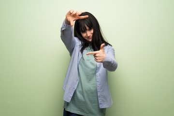 Young woman over green wall focusing face. Framing symbol