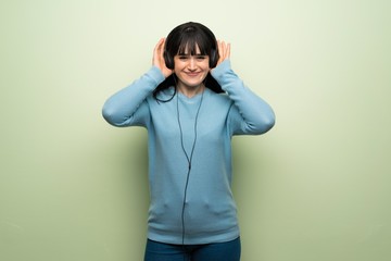 Young woman over green wall listening to music with headphones