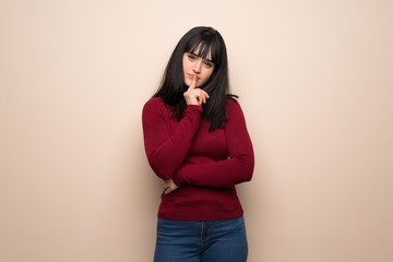 Young woman with red turtleneck showing a sign of silence gesture putting finger in mouth