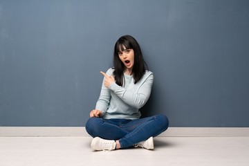 Woman sitting on the floor surprised and pointing side