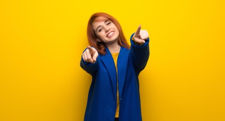 Young redhead woman with trench coat points finger at you while smiling