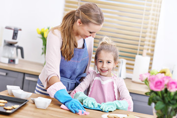 Little girl and her mom in aprons cleaning the kitchen