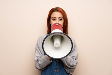 Young redhead woman over isolated background shouting through a megaphone