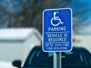 Handicapped parking sign with car, building and tree in snow covered parking lot in winter. Bokeh background.