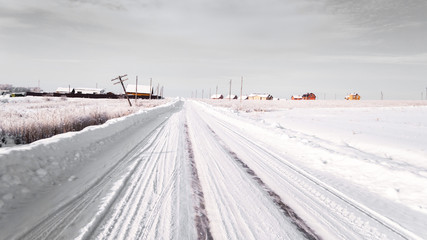 winter road. snow and ice. tire tracks. remote place, farm houses and fields covered with snow. Photo in gray tones