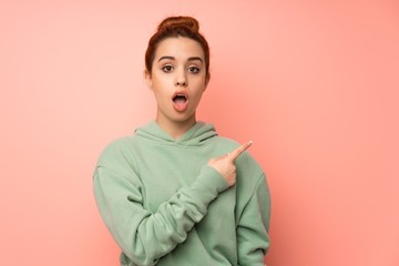 Young redhead woman with sweatshirt surprised and pointing side