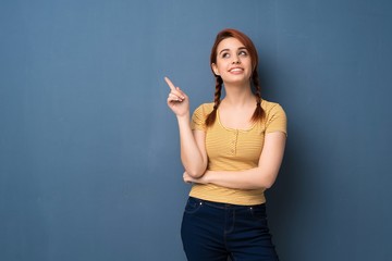 Young redhead woman over blue background pointing a great idea and looking up