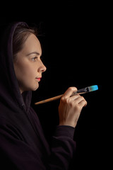 Obraz premium Portrait pensive artist painter girl in black hood posing with brush in a studio. isolated on black
