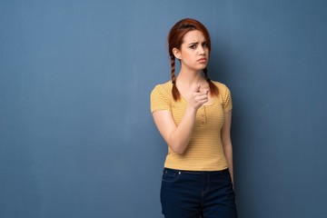 Young redhead woman over blue background serious and pointing to the front