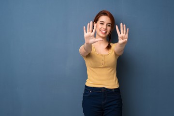 Young redhead woman over blue background counting nine with fingers