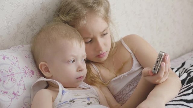Adorable little brother and sister using digital tablet, smiling and looking happy. Brother and sister having fun at home.