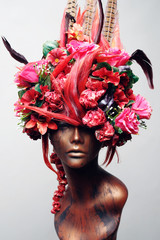 Decorated head of mannequin with hair, flowers and feathers, grey studio background