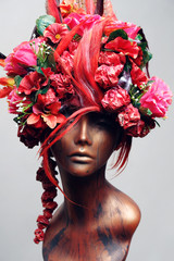Decorated head of mannequin with hair, flowers and feathers, grey studio background