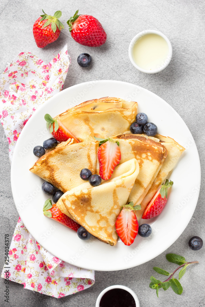 Wall mural Thin pancakes with strawberries and blueberries, jam, condensed milk, delicious Breakfast. Russian traditional dessert for Shrovetide celebration (maslenitsa). French crepes