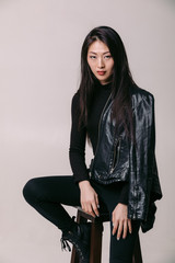 Fashionable asian model in black leather jacket posing in studio