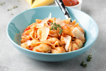 Pasta conchiglioni (conchiglie, shells) with tomato sauce, Parmesan cheese and thyme in a blue plate on a gray background. Delicious healthy vegetarian food, Italian cuisine