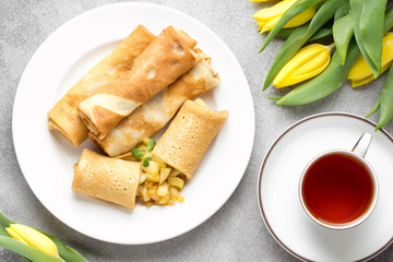 Thin pancakes (crepes) with apple filling, stuffed rolls, Russian traditional food for maslenitsa, French dessert, breakfast with tulips on mother's day