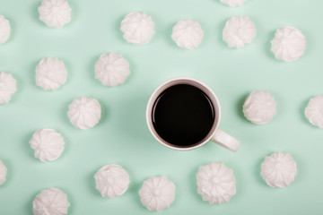 Obraz na płótnie Canvas Cup of coffee with macaron meringue on turquoise background from above, flat lay