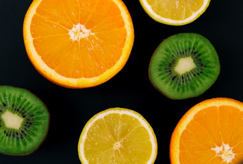 Slices of kiwi, lemon and orange on a black background, on a chalk board. There is a place for text.
