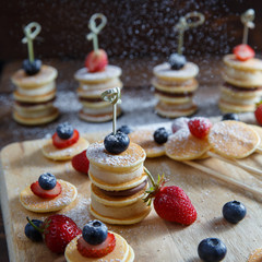 Fruit, berry and pancake canapes on white wooden table