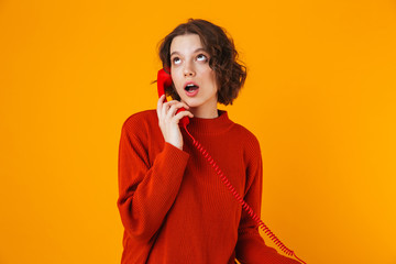 Serious young pretty woman posing isolated over yellow wall background talking by telephone.