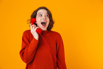 Emotional young pretty woman posing isolated over yellow wall background talking by telephone.