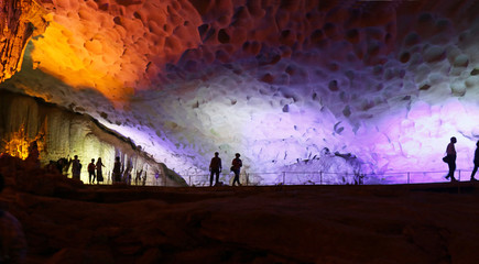 Ha Long Bay, Vietnam.  Silhouette of Tourists walking in Illuminated Cave. Limestone  Rock Formations.