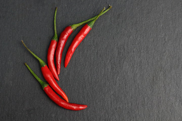 Group of hot spice red chilli fresh cayenne pepper on a black graphite slate stone surface. Natural...
