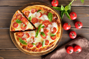 Appetizing pizza Margherita on a cutting board, fresh tomatoes and basil