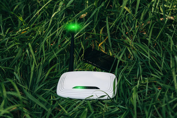 Wi-Fi router and smartphone standing in the green grass. Internet connection in the nature. Forest...