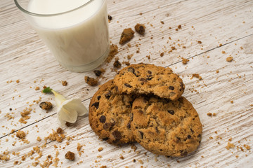 Top view of chocolate chip cookies, crumbs and a glass of milk on a wooden table