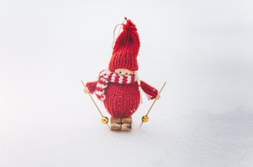 Winter photo with Christmas decorations for pine tree. Knitted snowman toy girl standing on the ski in the forest. Happy holidays ornaments postcard. Snowy weather.