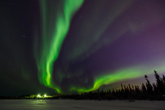 Bright green flashes of northern lights go into perspective beyond black horizon