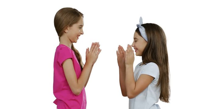 Two friends schoolgirls standing face to face on the white screen background and playing hands game.